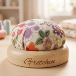 Personlig, färgglad nåldyna i vintagestil med blommönster, graverat namn och träfot – ett sömnadshantverk som födelsedagspresent till skräddare och hantverkare